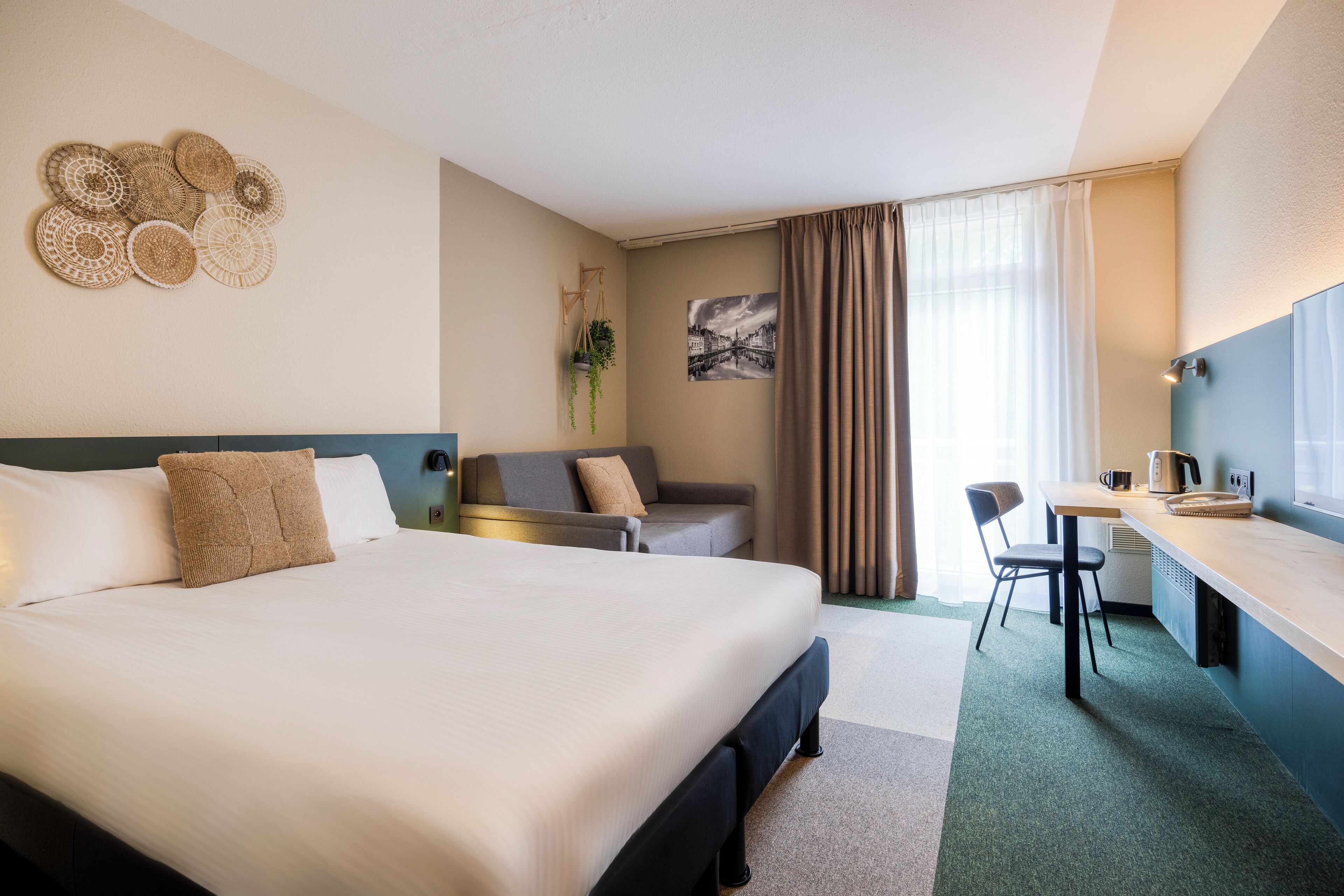 Une chambre d’hôtel avec un grand lit, un bureau, une chaise, un canapé et une plante fixée au mur.