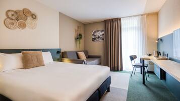 Une chambre d’hôtel avec un grand lit, un bureau, une chaise, un canapé et une plante fixée au mur.