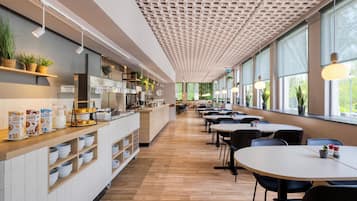Ein modernes Café mit einer langen Theke, Regalen mit Pflanzen und Tischen mit Stühlen.