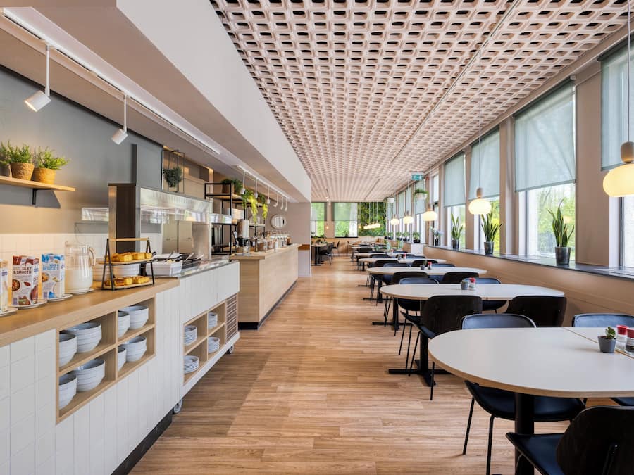 Um café moderno com um balcão comprido, prateleiras com plantas e mesas com cadeiras.