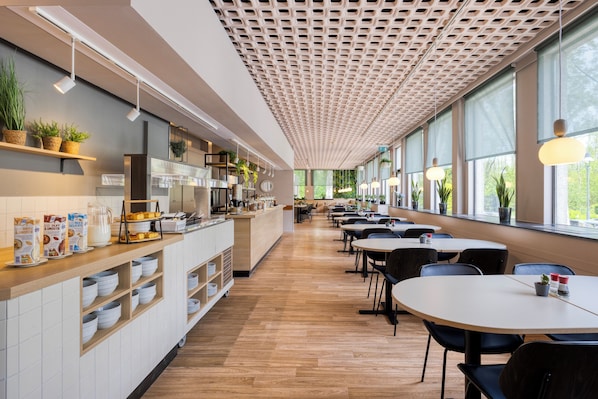 Una cafetería moderna con una barra larga, estantes con plantas y mesas con sillas.
