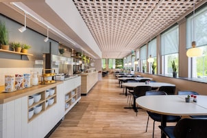 Una cafetería moderna con una barra larga, estantes con plantas y mesas con sillas.
