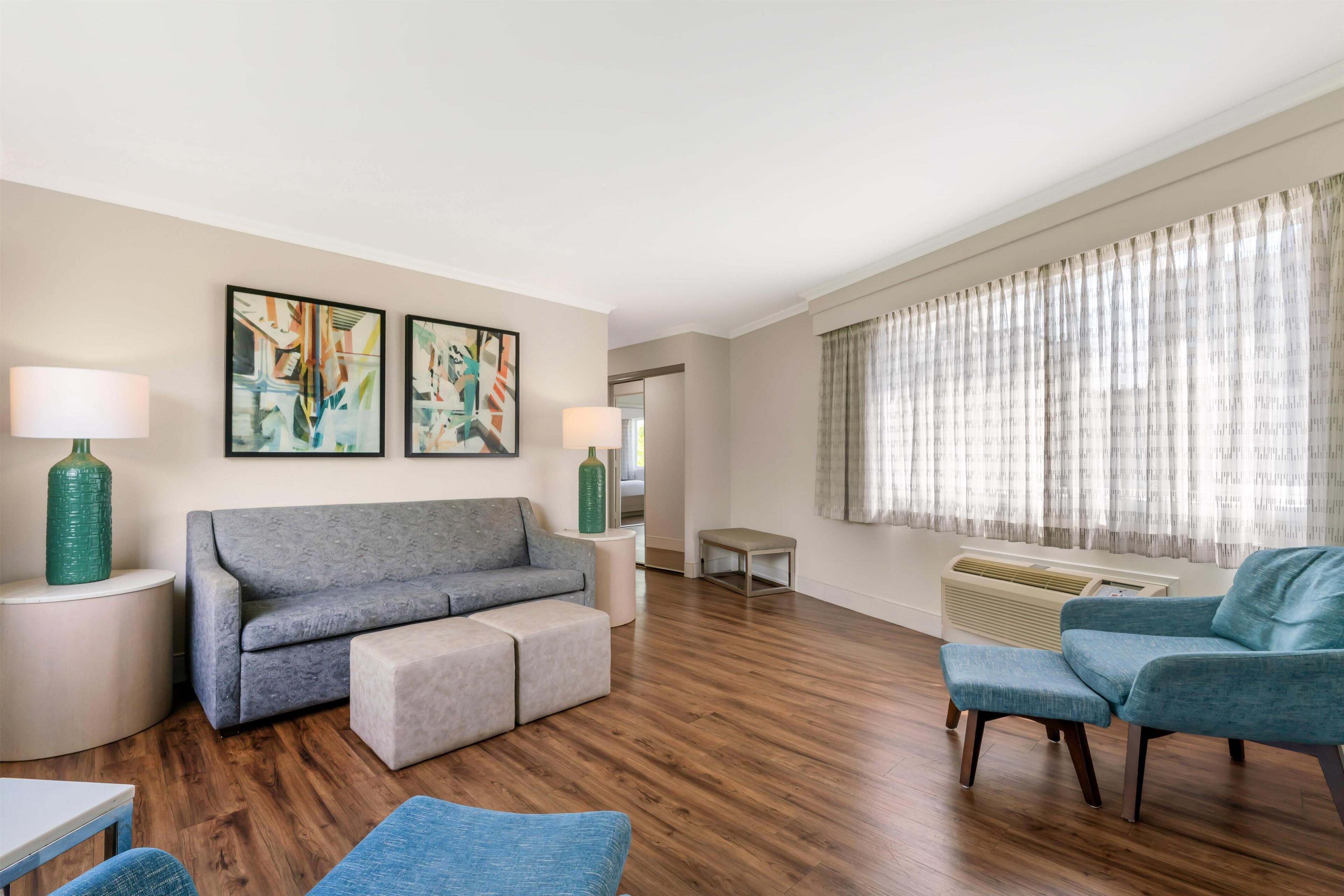 Una sala de estar moderna con un sofá gris, un reposapiés y un sillón azul, una mesa de centro redonda y dos mesitas de noche con lámparas.