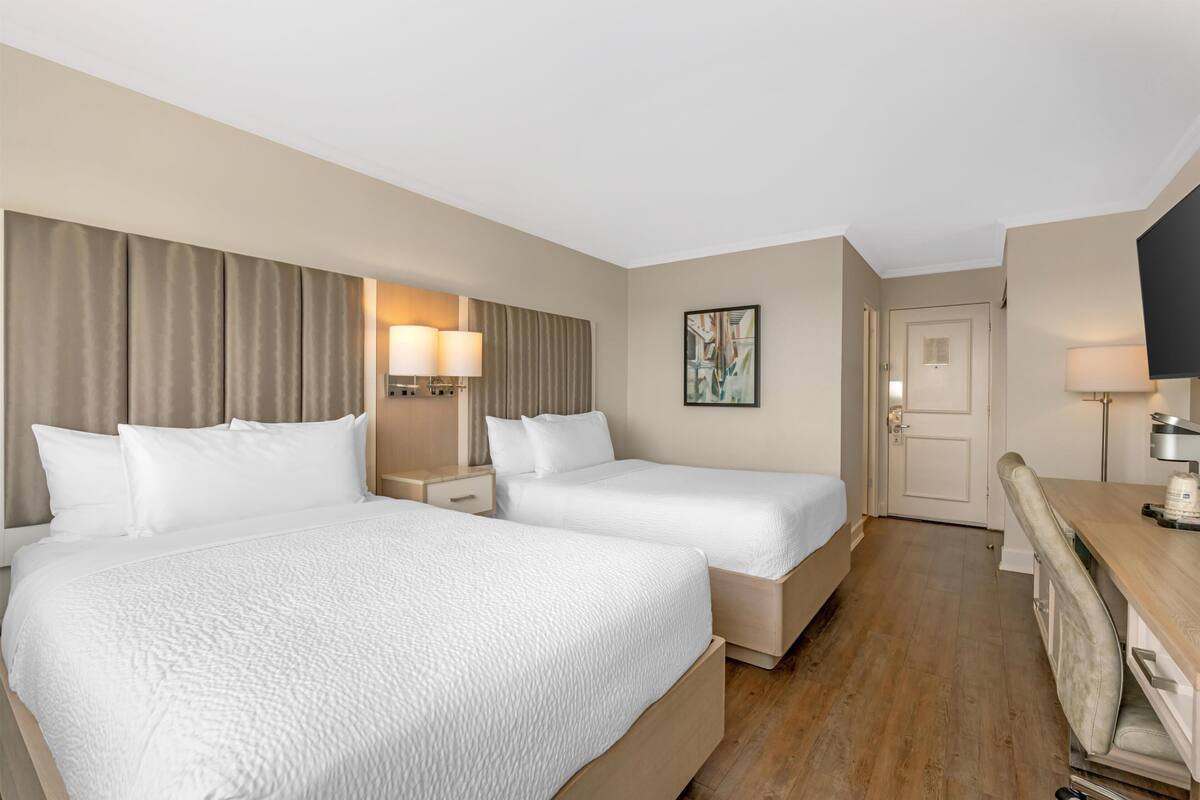 Ein Hotelzimmer mit zwei Betten, einem Schreibtisch, einem Stuhl, einem Fernseher und einer Tür.