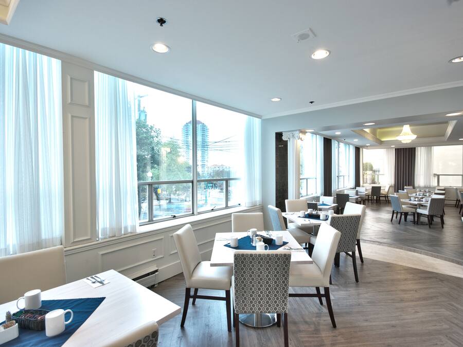 Un amplio comedor de hotel con grandes ventanales, varias mesas y sillas.