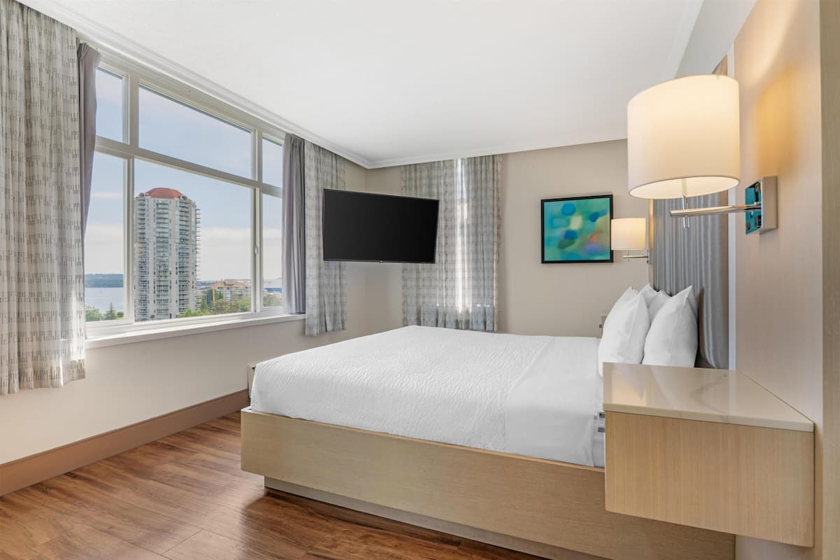 Ein Hotelzimmer mit Bett, Fernseher, einem Gemälde und einem Fenster mit Vorhängen.