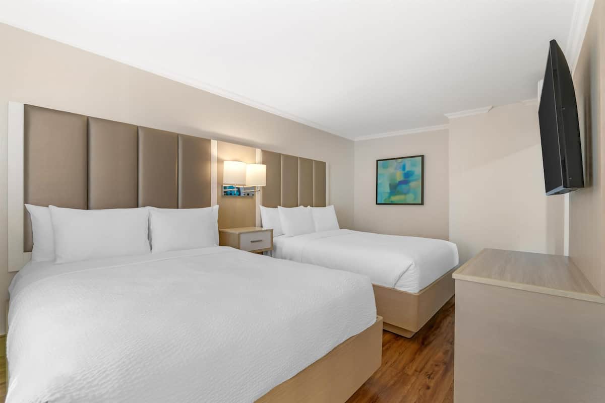 Ein Hotelzimmer mit zwei Betten, einem Nachttisch, einer Lampe, einem Flachbildfernseher und einem Gemälde an der Wand.