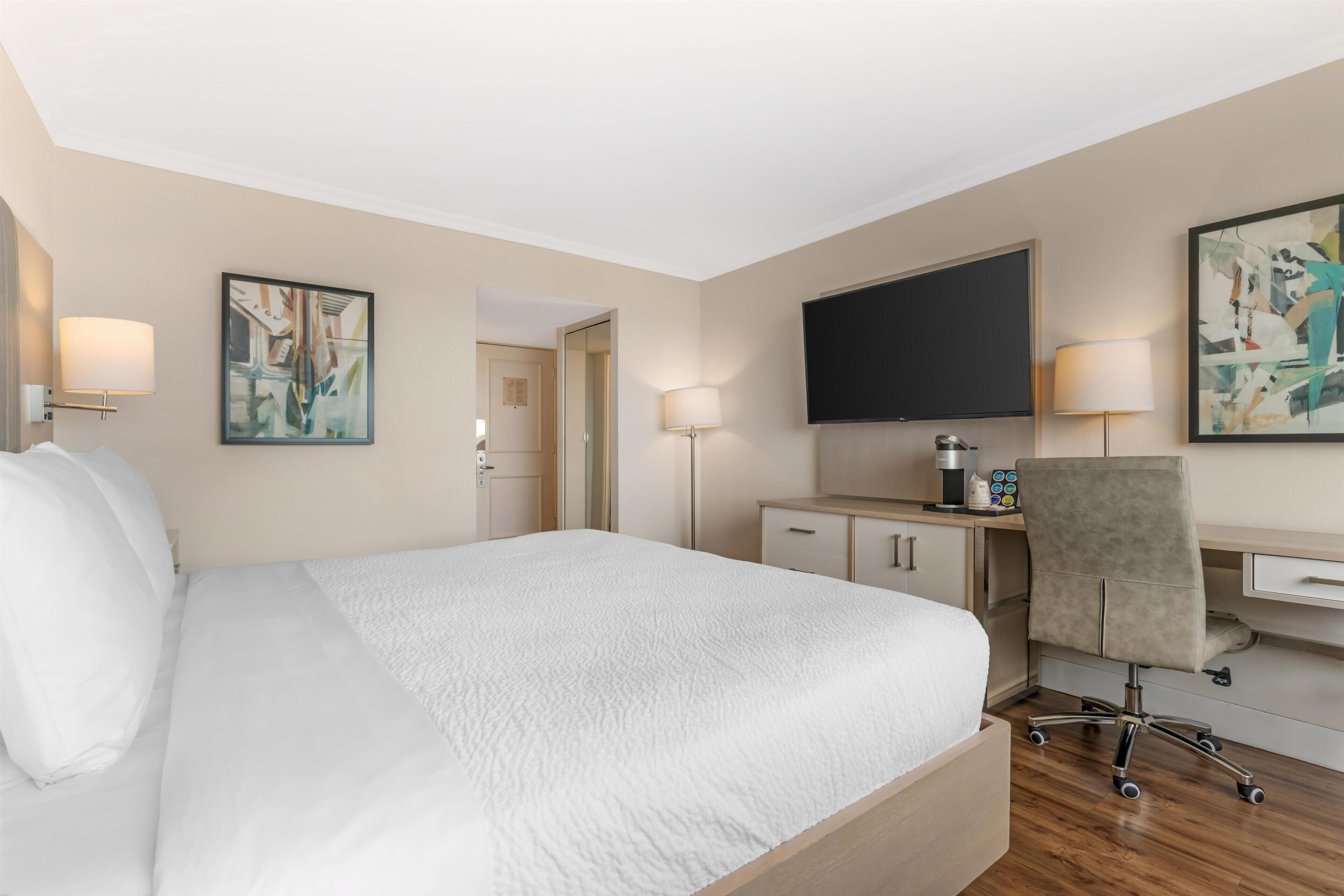 Une chambre d’hôtel équipée d’un lit, d’un bureau, d’une chaise, d’une télévision et d’œuvres d’art.