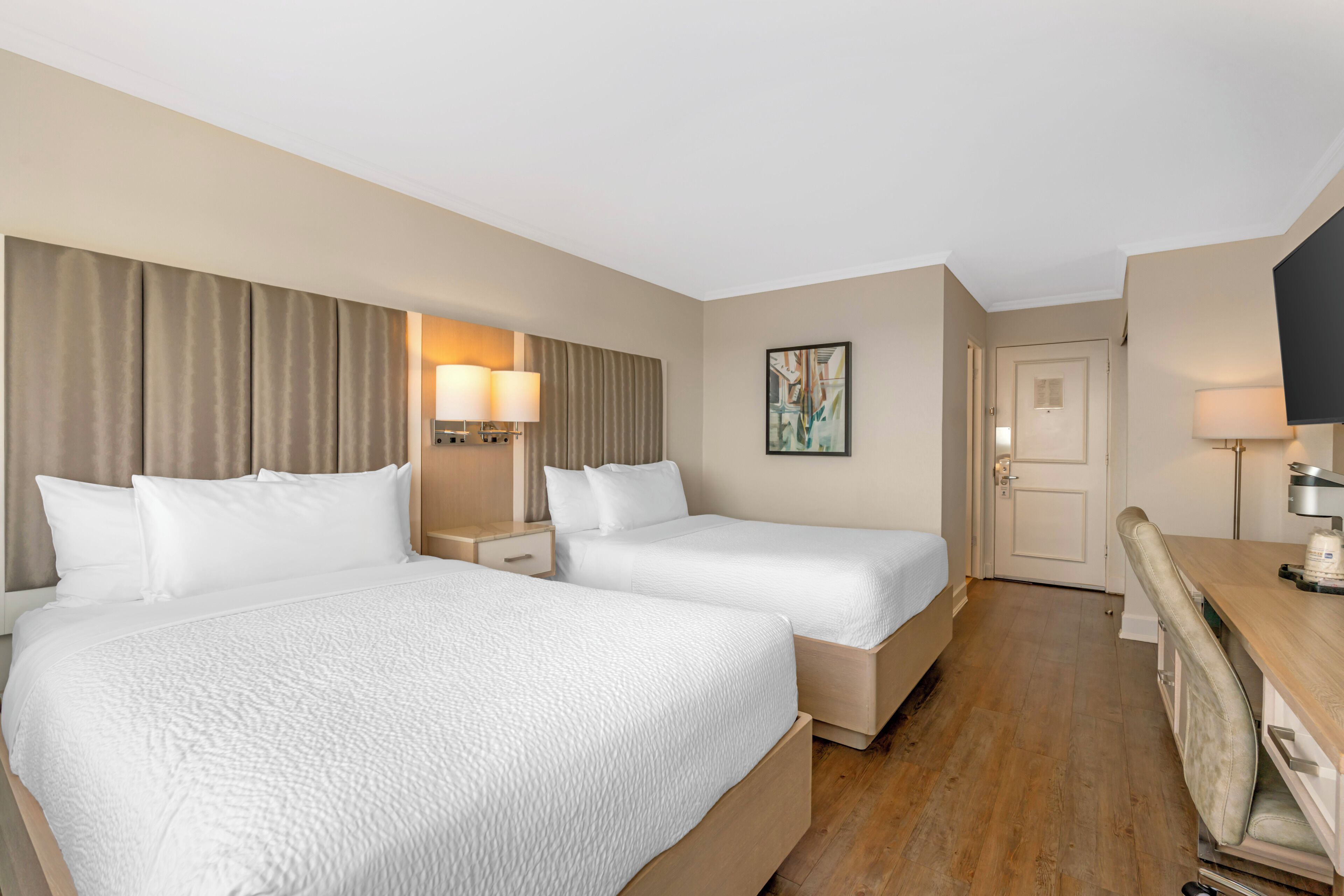 A hotel room with two beds, a desk, a TV, and a door.