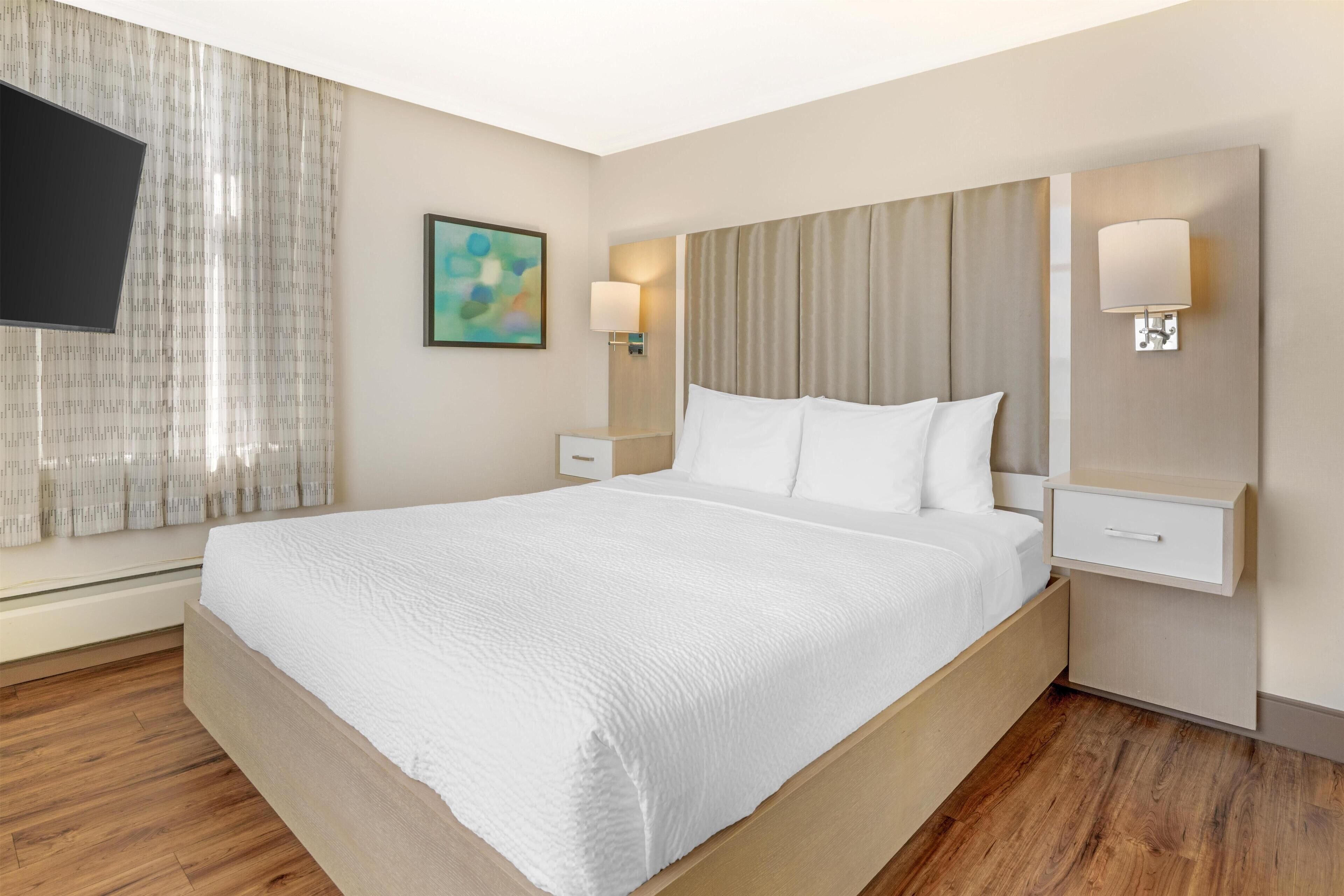 A hotel room with a large bed, wooden flooring, a flat-screen TV, and a painting on the wall.