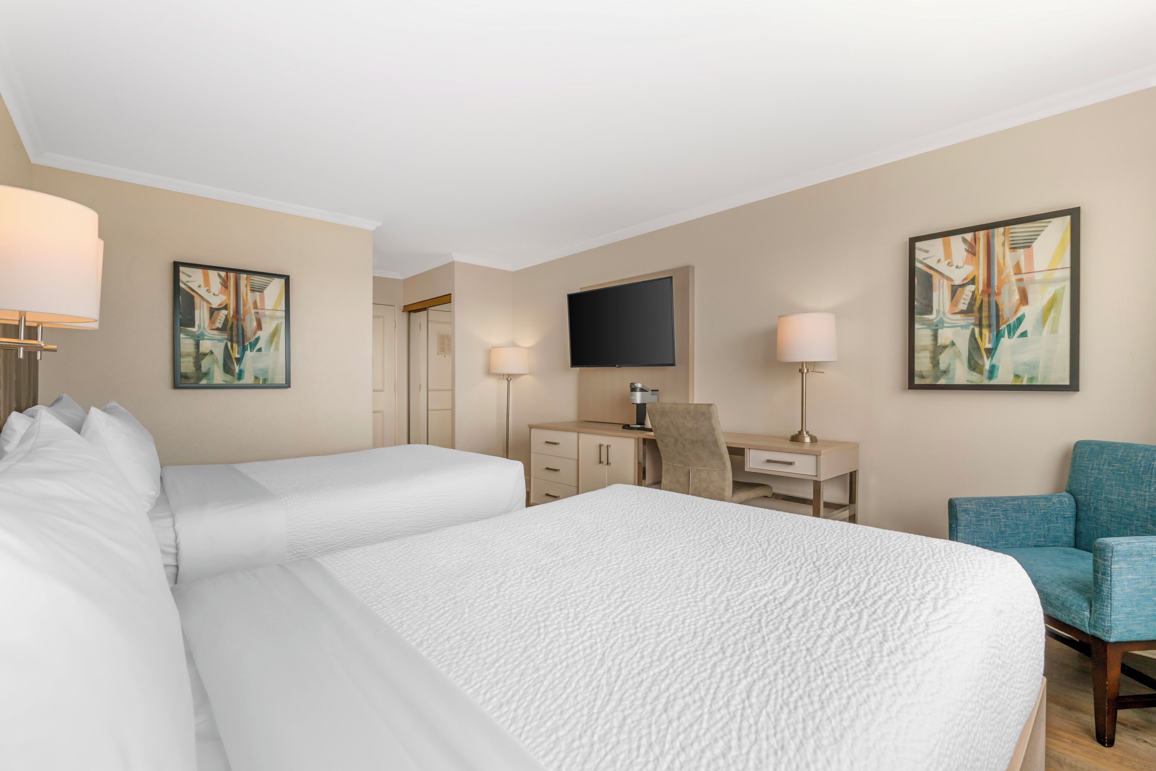 A hotel room with a large bed, a desk, a chair, a TV, and artwork on the walls.
