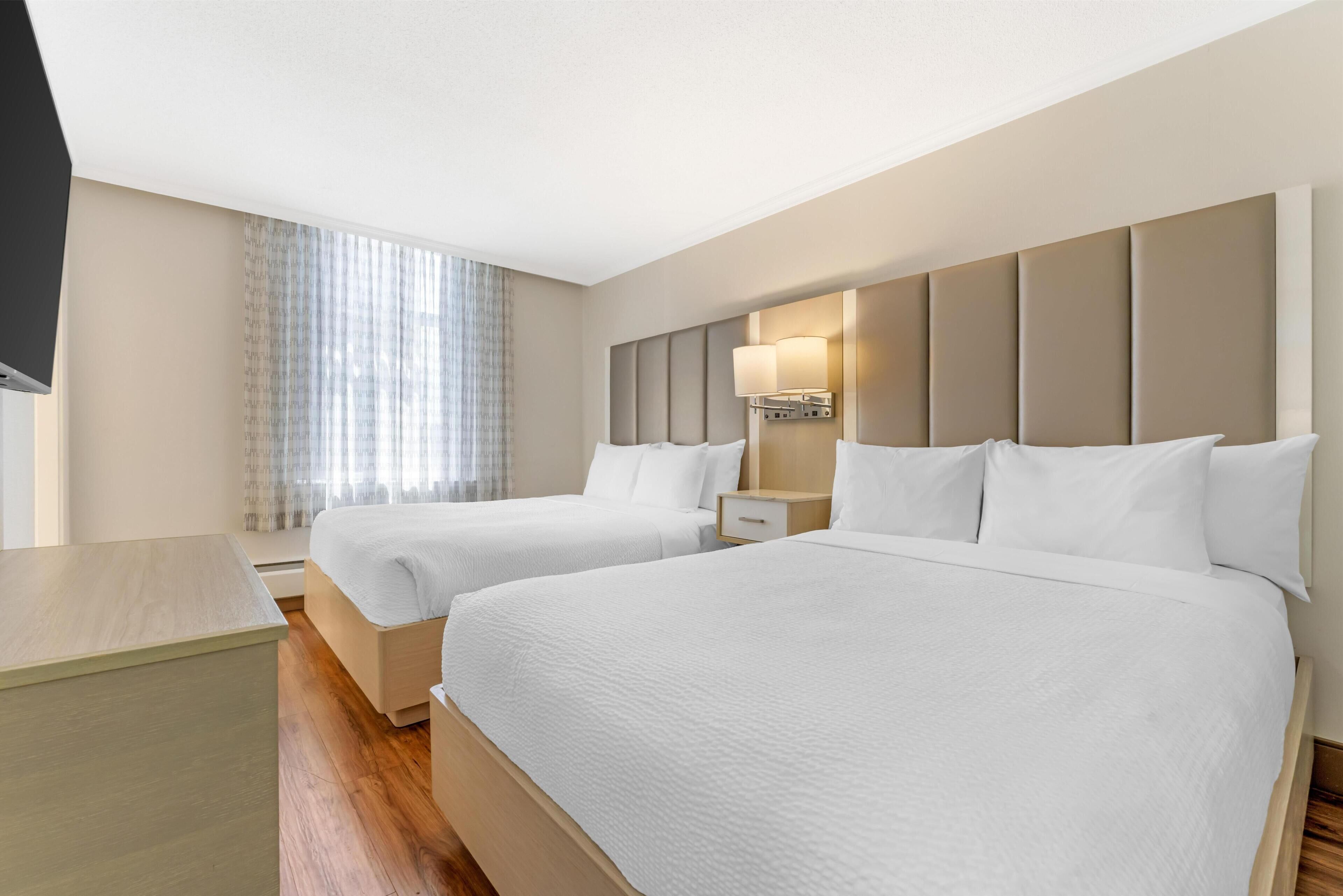 A hotel room with two beds, a TV, a bedside table, and a window with curtains.