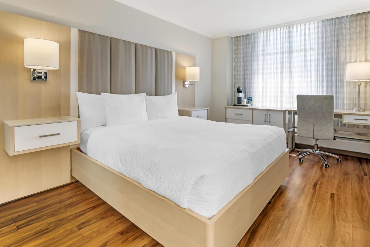 Ein Hotelzimmer mit einem großen Bett, Nachttischen, einem Schreibtisch mit Stuhl und einem fenster mit Vorhängen.