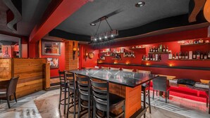 Un espace bar doté d’un long comptoir, de plusieurs options d’assises, notamment des banquettes et des tabourets hauts, et d’une variété de bouteilles exposées sur des étagères.