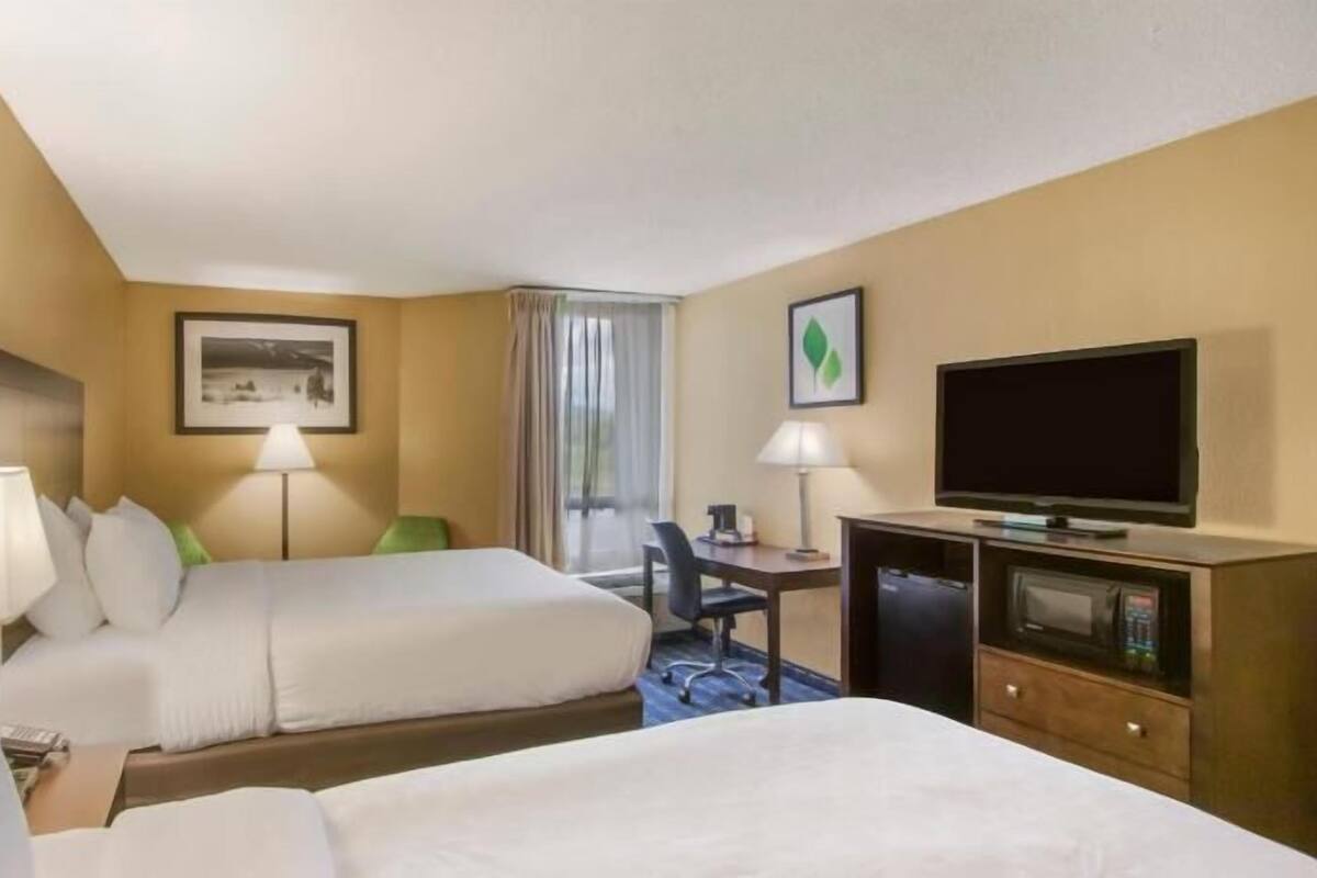 A hotel room with two beds, a desk, a television, and a window with curtains.