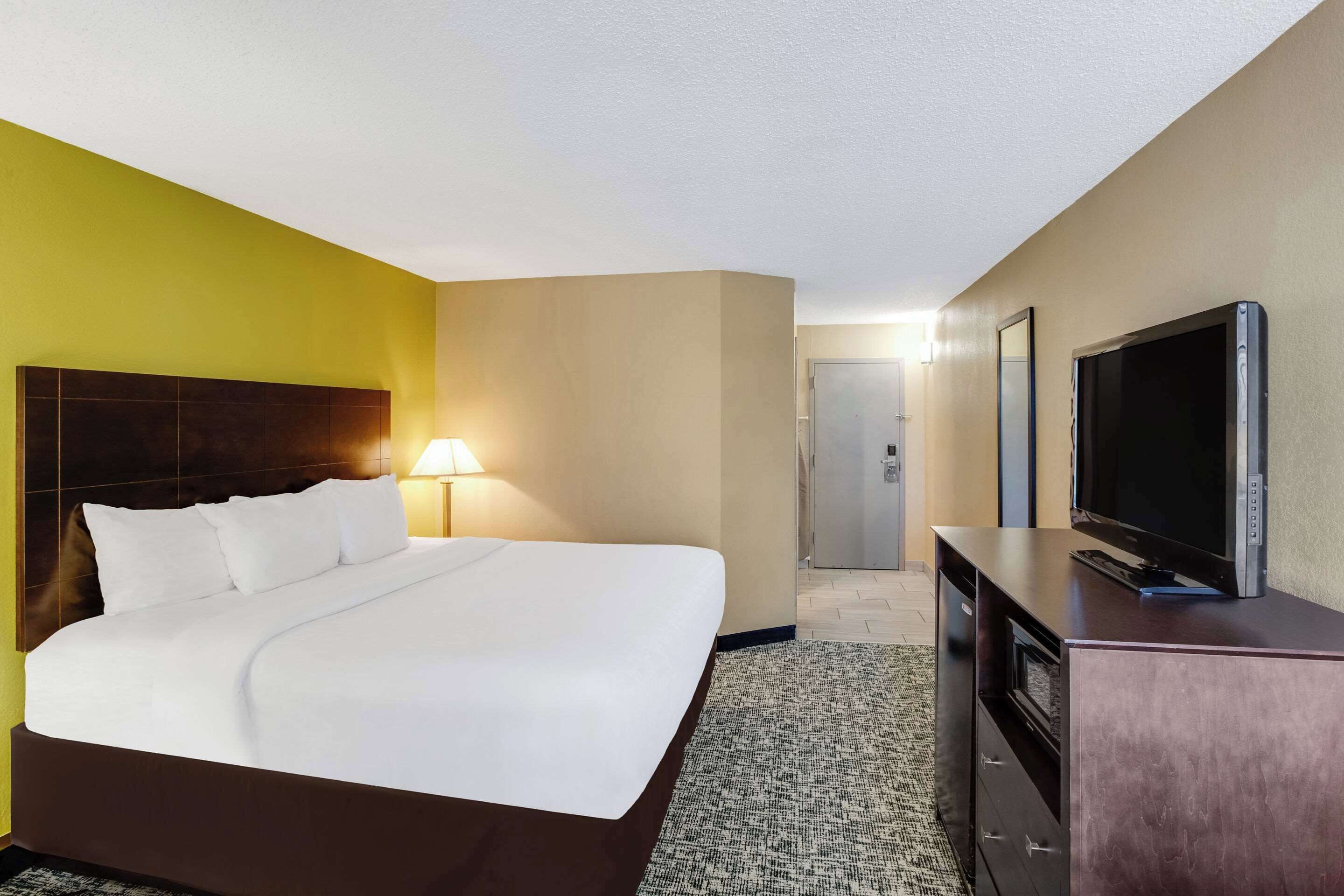A hotel room with a bed, a television on a dresser, and a door leading to a hallway.