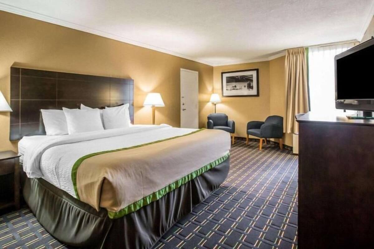 A hotel room with a bed, two chairs, a desk, a television, and a framed picture on the wall.