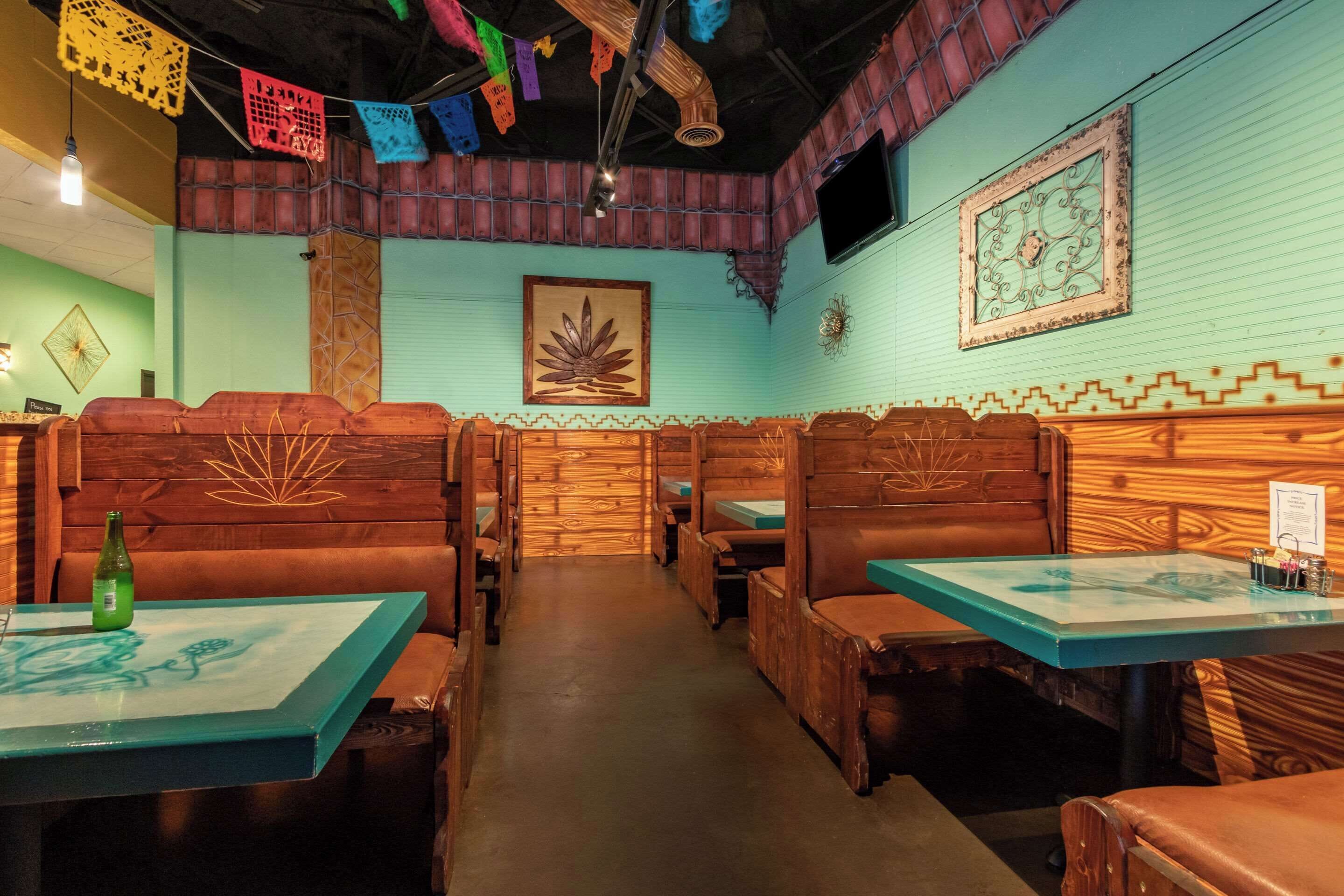 Un restaurante con cabinas y mesas de madera, farolillos de papel de colores y un mural en la pared.