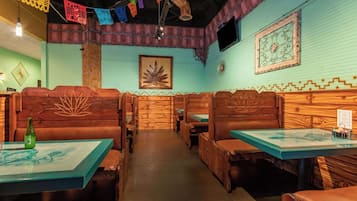 Un restaurante con cabinas y mesas de madera, farolillos de papel de colores y un mural en la pared.
