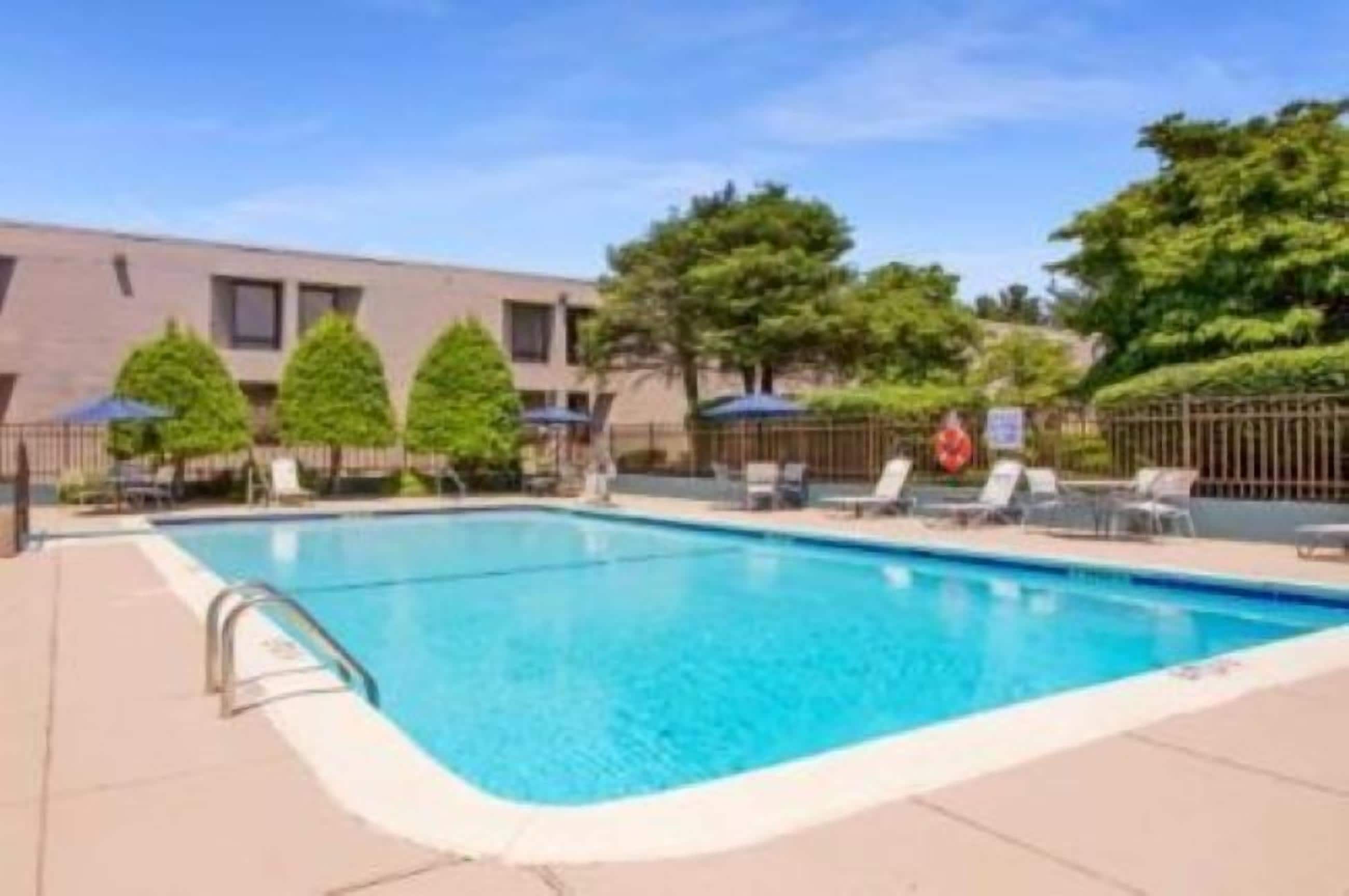 Piscina retangular com escada de metal, rodeada por espreguiçadeiras e guarda-sóis.