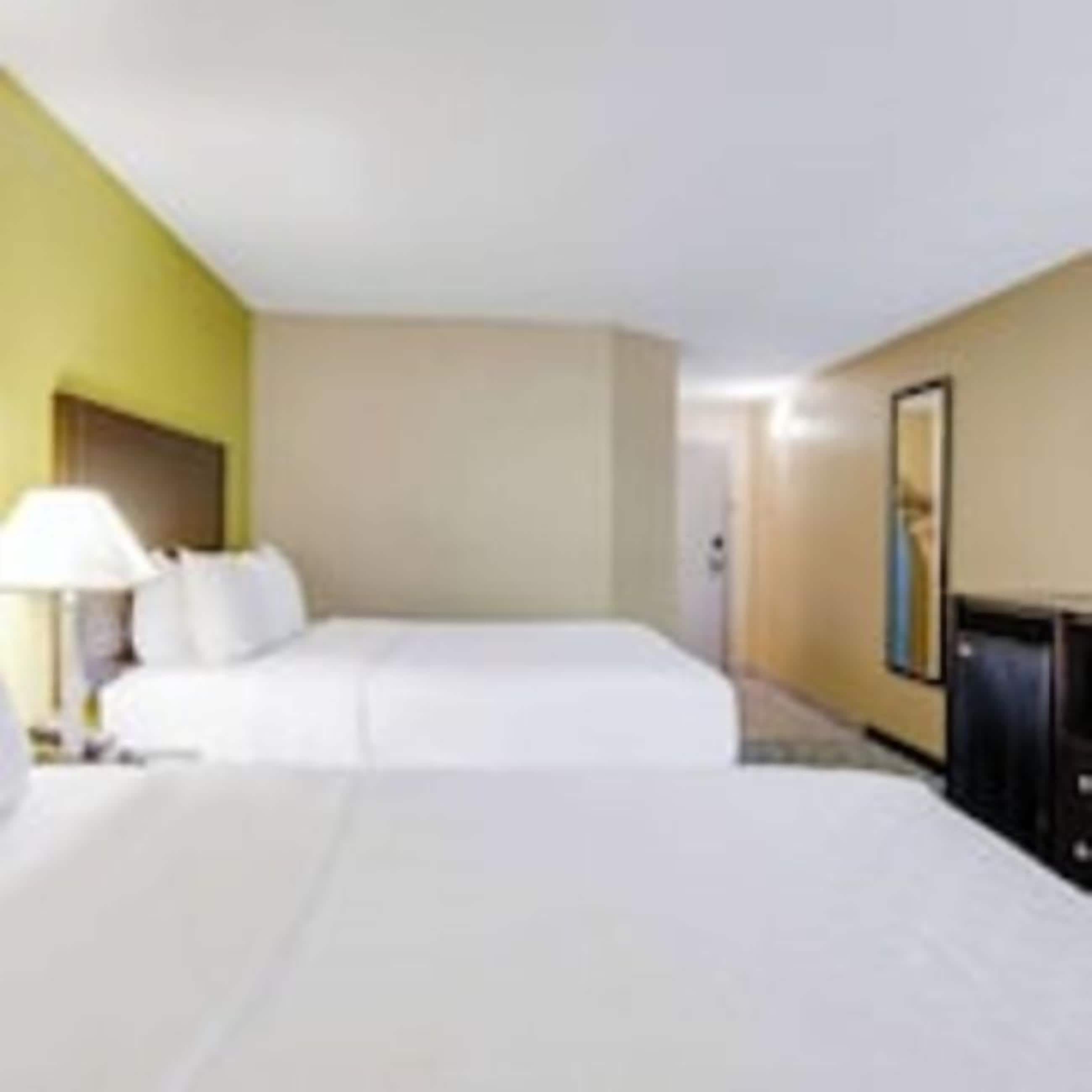 Una habitación de hotel con cama, mesita de noche, lámpara y televisor de pared.
