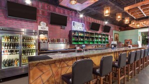 Zona de bar con un letrero de neón de Bud Light, un refrigerador lleno de bebidas y una barra con taburetes.