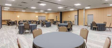 A conference room with multiple tables and chairs, equipped with a whiteboard and presentation screen.
