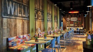 A restaurant interior with wooden walls, a long counter with tables and chairs, and a colorful bench seating area. - Graduate by Hilton Oxford (Oxford)