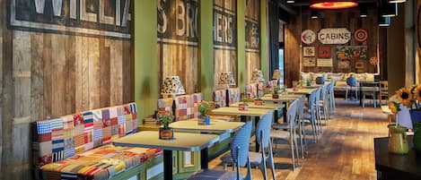 A restaurant interior with wooden walls, a long counter with tables and chairs, and a colorful bench seating area.