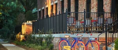 A blue bicycle with red wheels parked in front of a brick building with a black metal fence.
