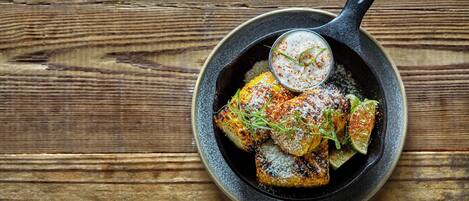 A skillet with grilled corn and lime wedges on a wooden surface.