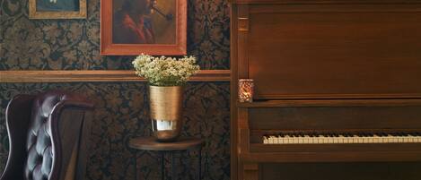 A room with a piano, a framed portrait, a wall-mounted poster, and a table with candles.