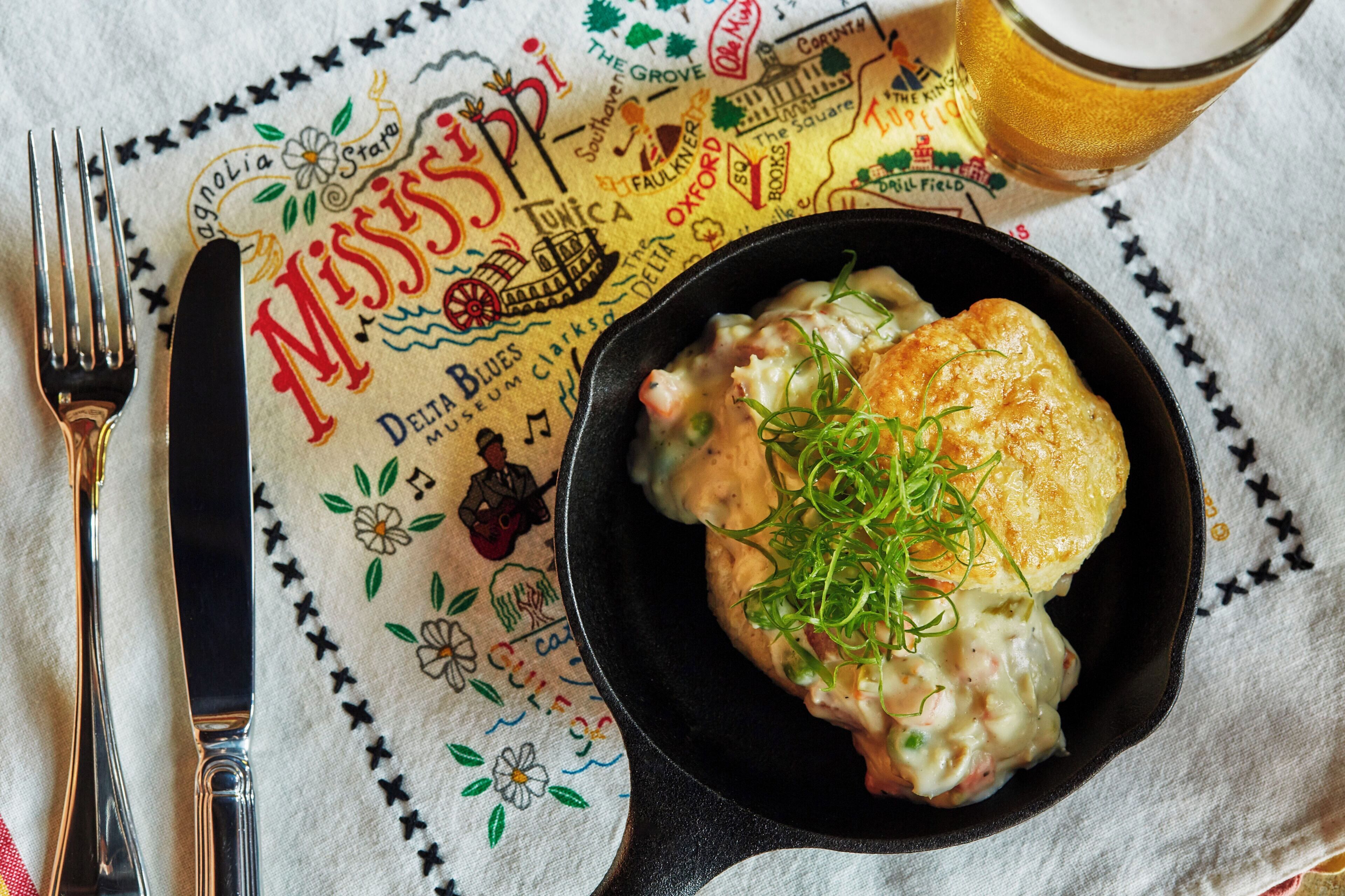 A meal with a biscuit and creamy sauce in a black bowl, placed on a tablecloth with a map design.