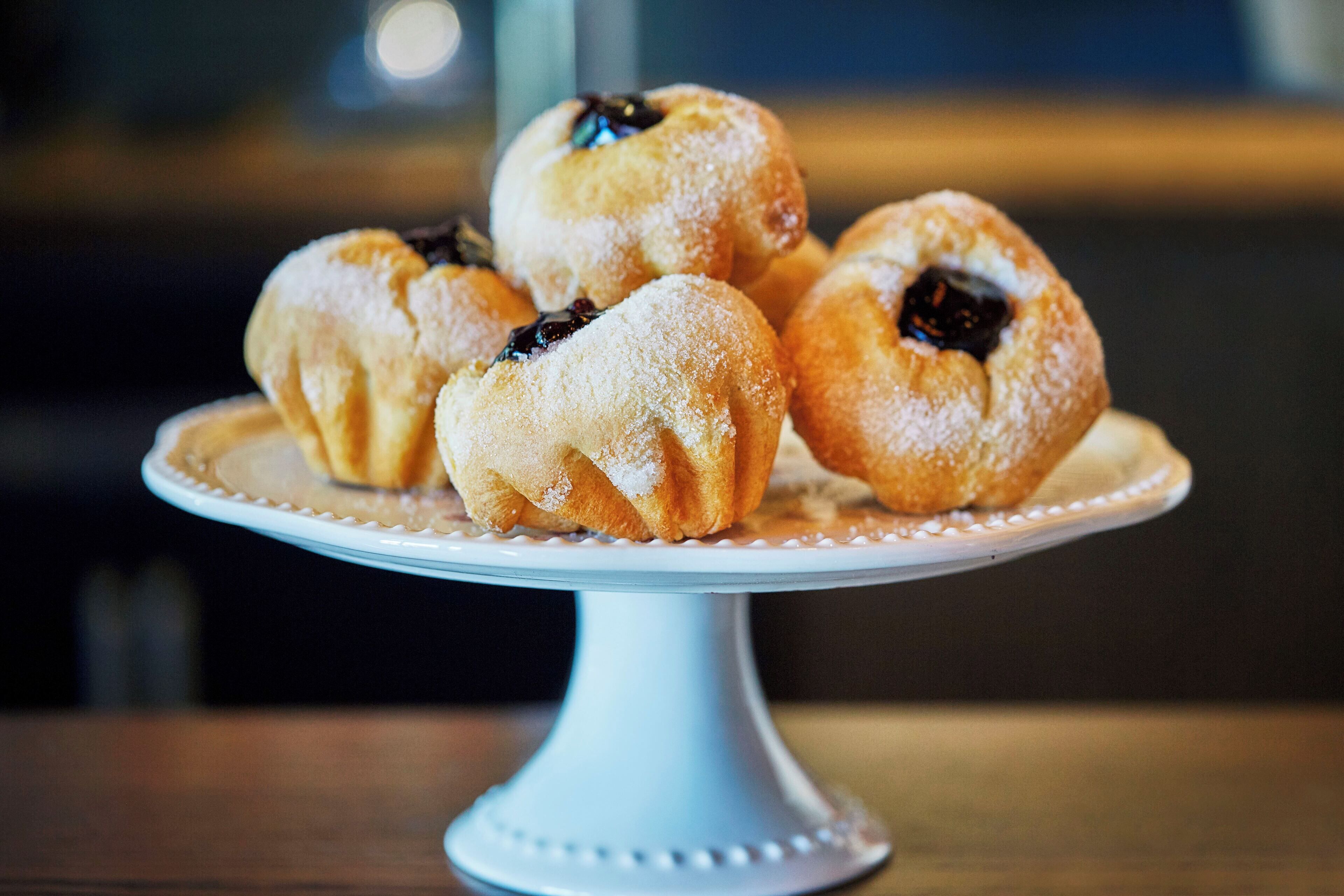A white cake stand with a plate holding several round pastries dusted with powdered sugar.