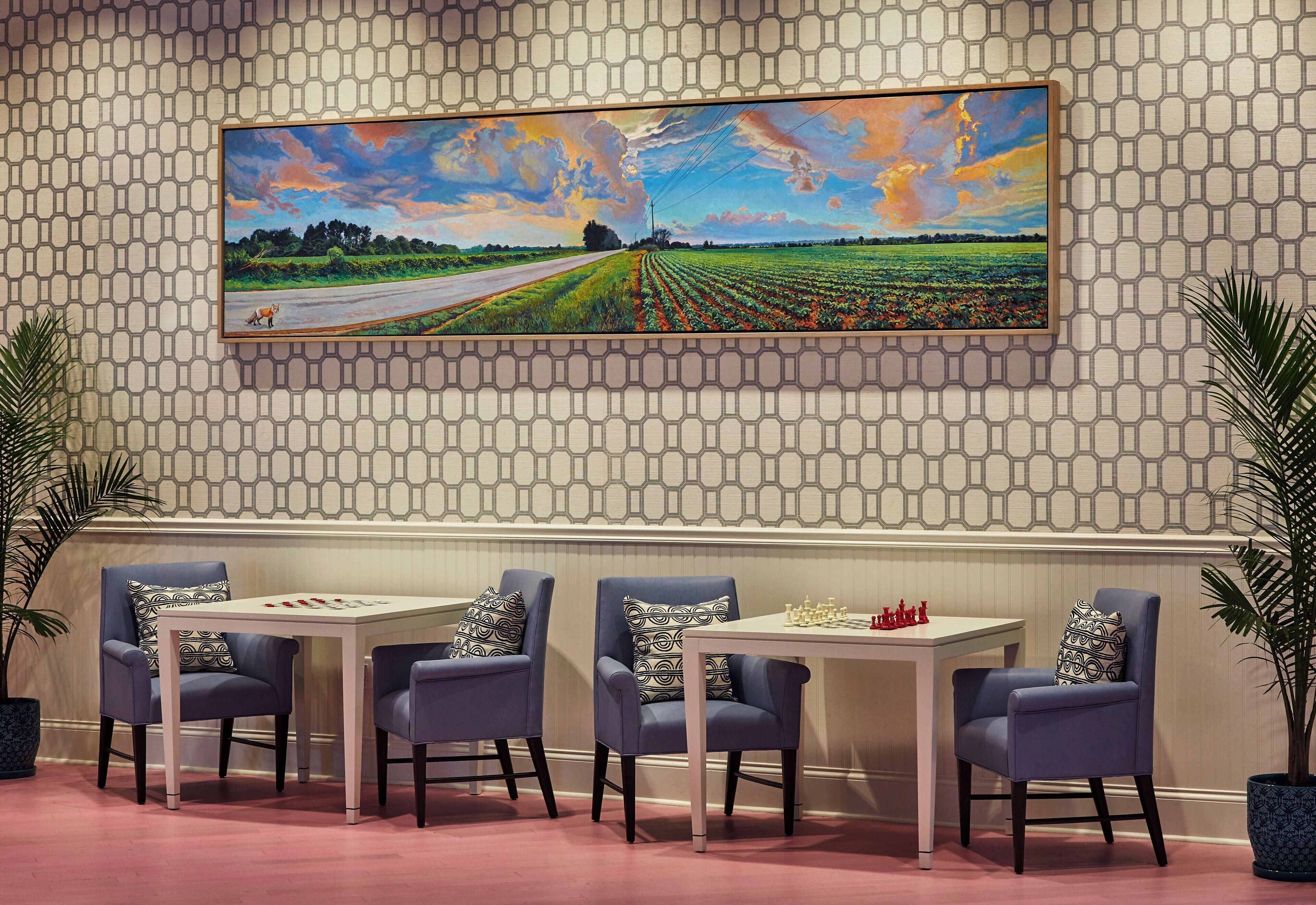 A dining area with a table and chairs, a painting on the wall, and a patterned wall.
