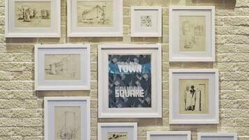 Una pared con múltiples bocetos y dibujos enmarcados, incluyendo uno que dice "TOWN SQUARE".