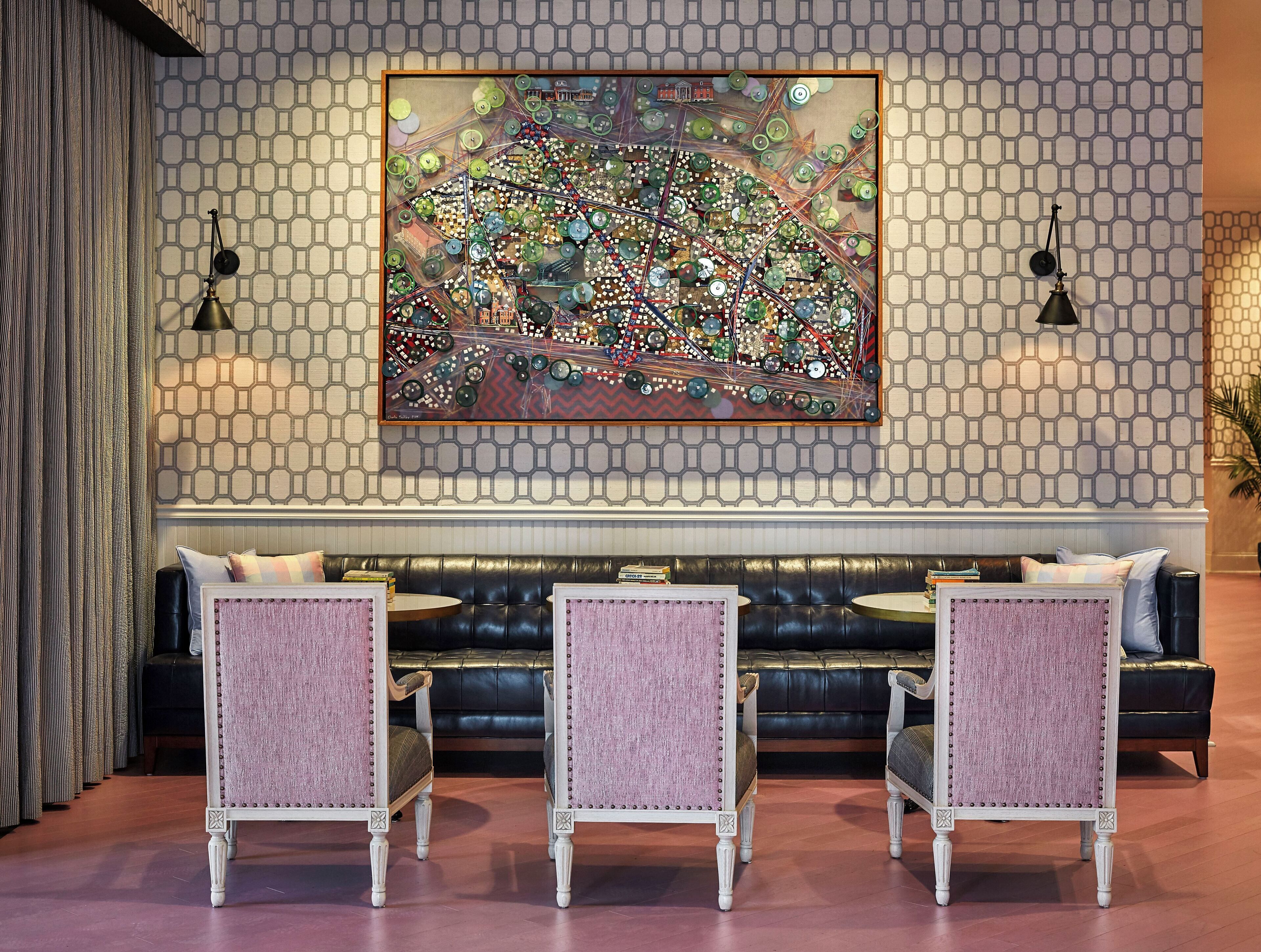 A lobby with a patterned wall, a large abstract painting, and three upholstered chairs with a cushioned bench in the background.