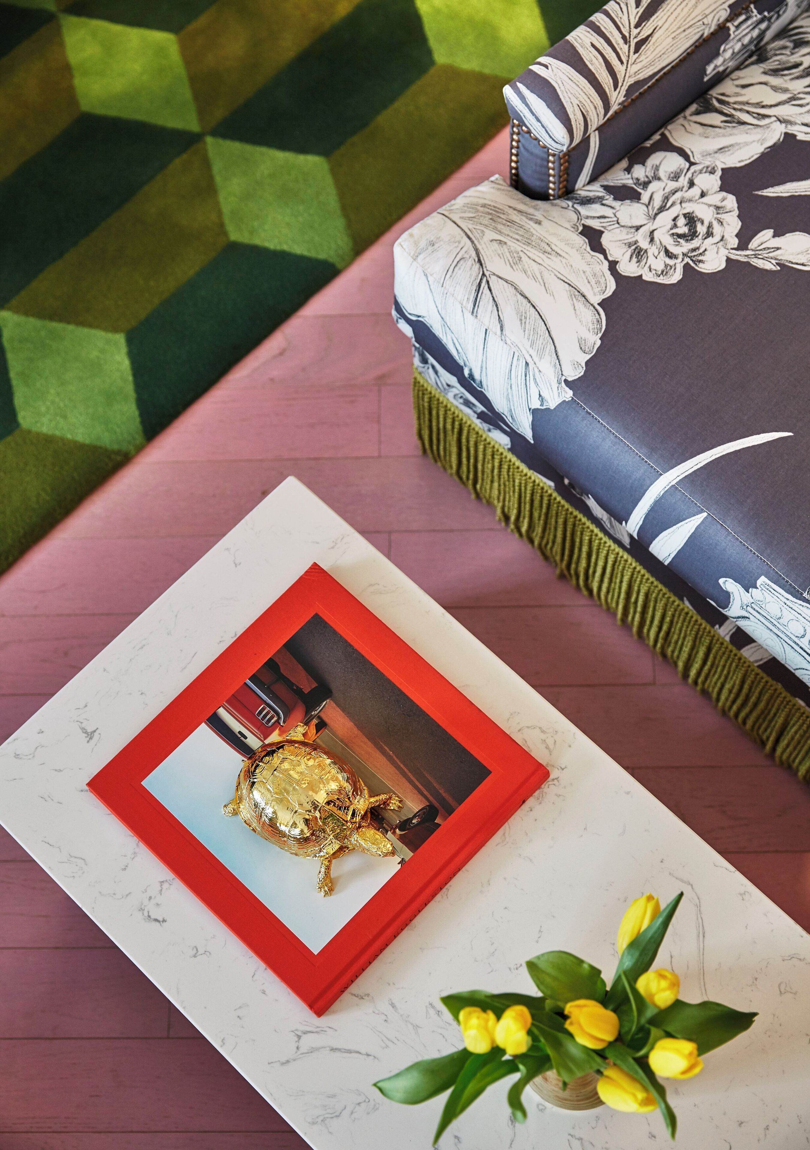 A framed picture of a turtle on a white surface, a small yellow flower arrangement, and a patterned sofa with a green and white cushion.