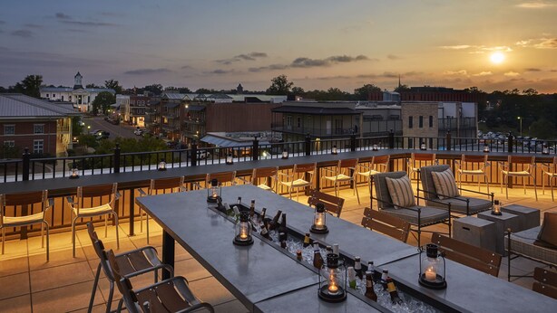 A rooftop bar with outdoor seating, ice buckets with bottles, and a sunset view. - Graduate by Hilton Oxford (Oxford)