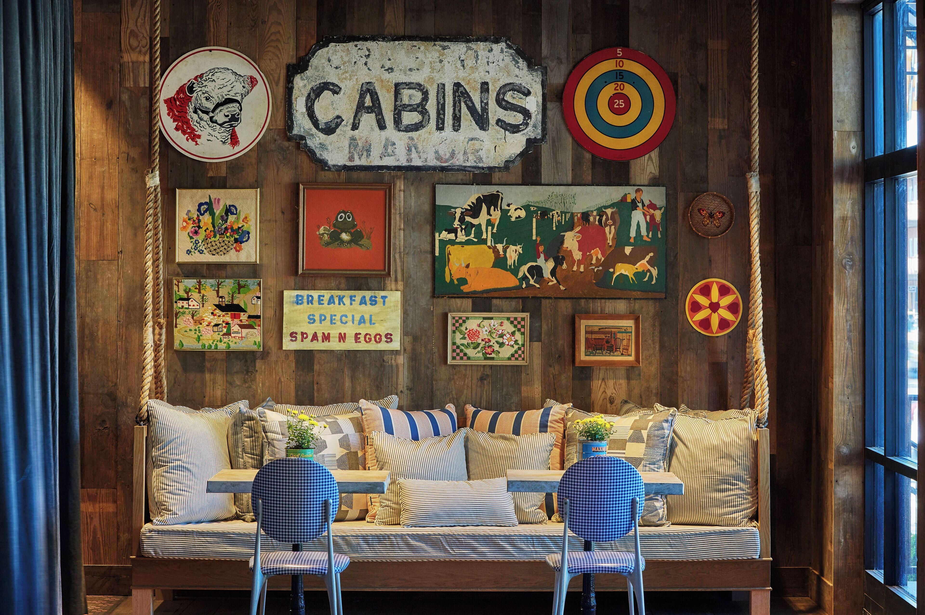 A rustic wooden interior with a sofa, chairs, and various wall decorations including a sign that reads "CABINS MANOR".