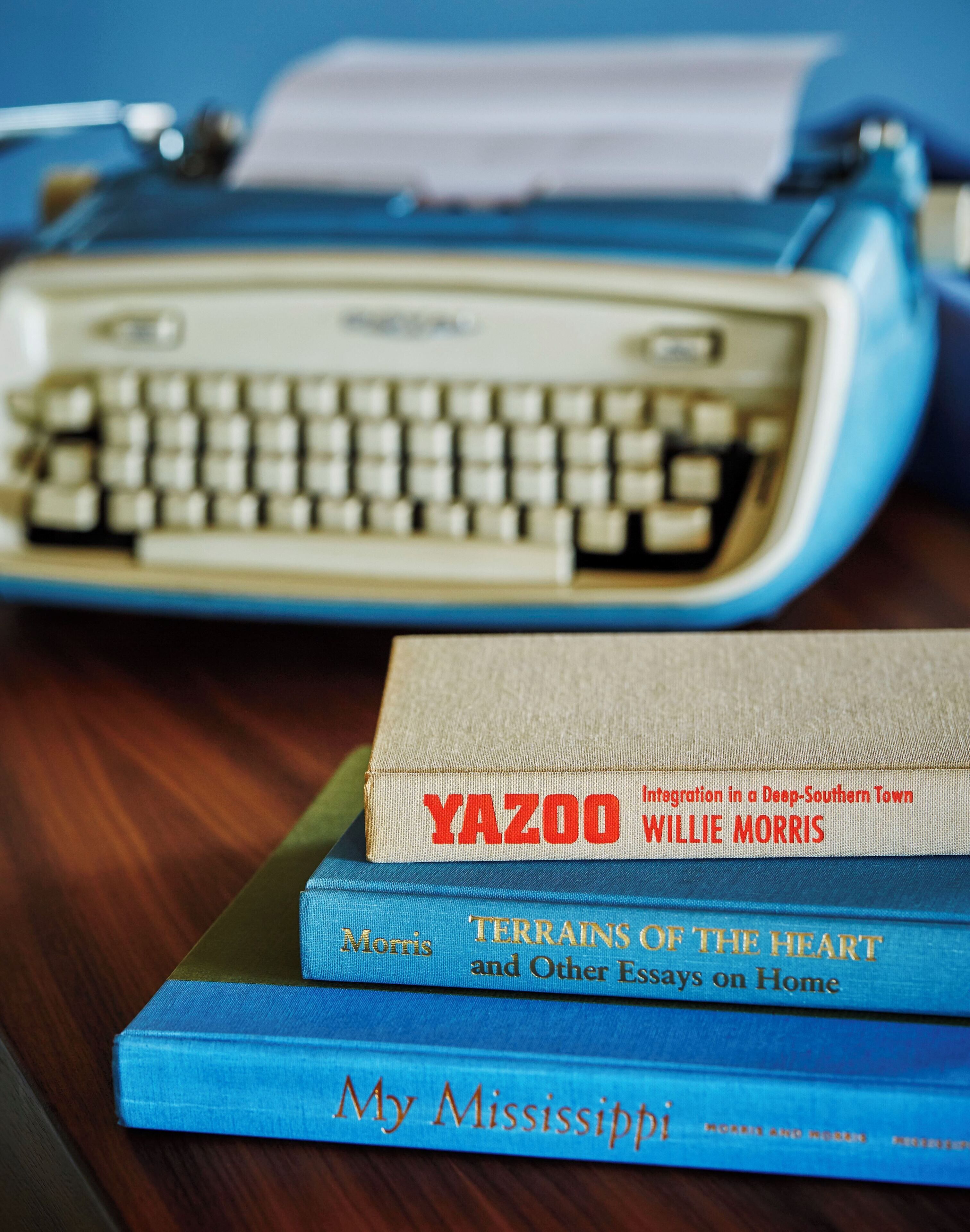 A typewriter with a stack of books on a wooden surface.