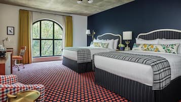 A hotel room with a large window, two beds with matching headboards, a red and black polka dot carpet, and a small seating area with a checkered sofa and a round table.