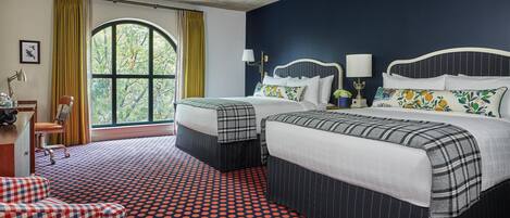 A hotel room with a large window, two beds with matching headboards, a red and black polka dot carpet, and a small seating area with a checkered sofa and a round table.