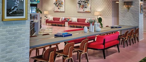 A modern living room with a long dining table, red sofas, and wooden chairs. There are bookshelves and a globe on the wall.