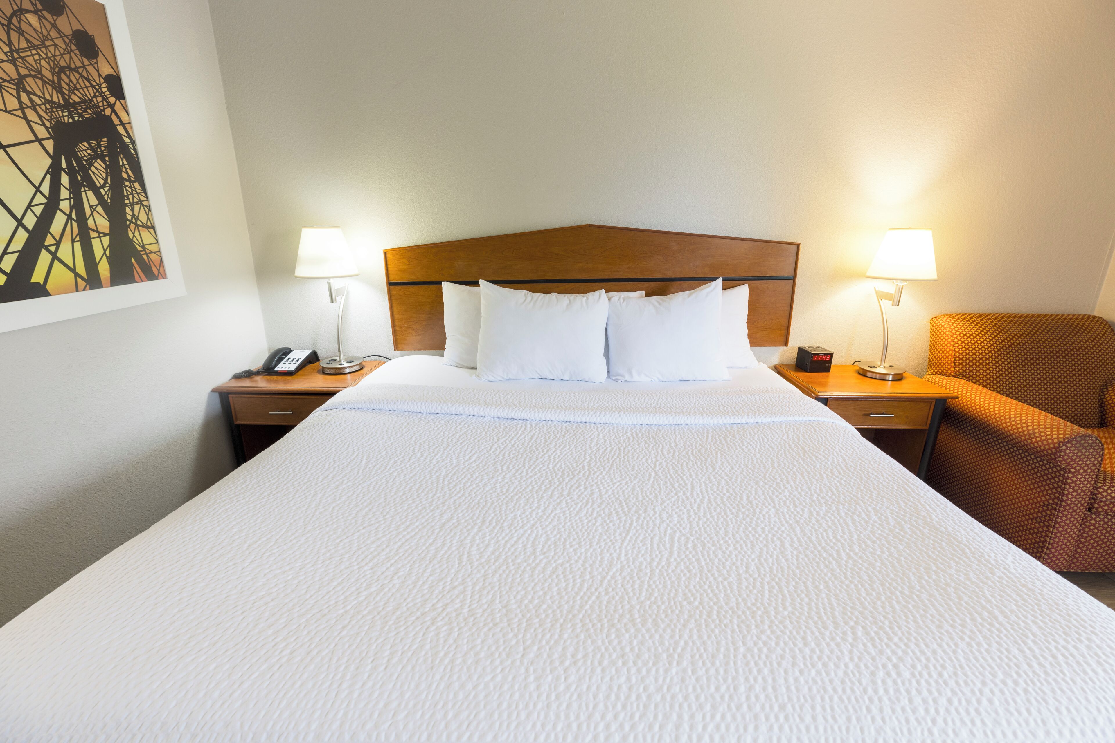 A hotel room with a large bed, two bedside tables, a nightstand, a lamp, and a chair.