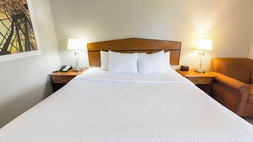 A hotel room with a large bed, two bedside tables, a nightstand, a lamp, and a chair.