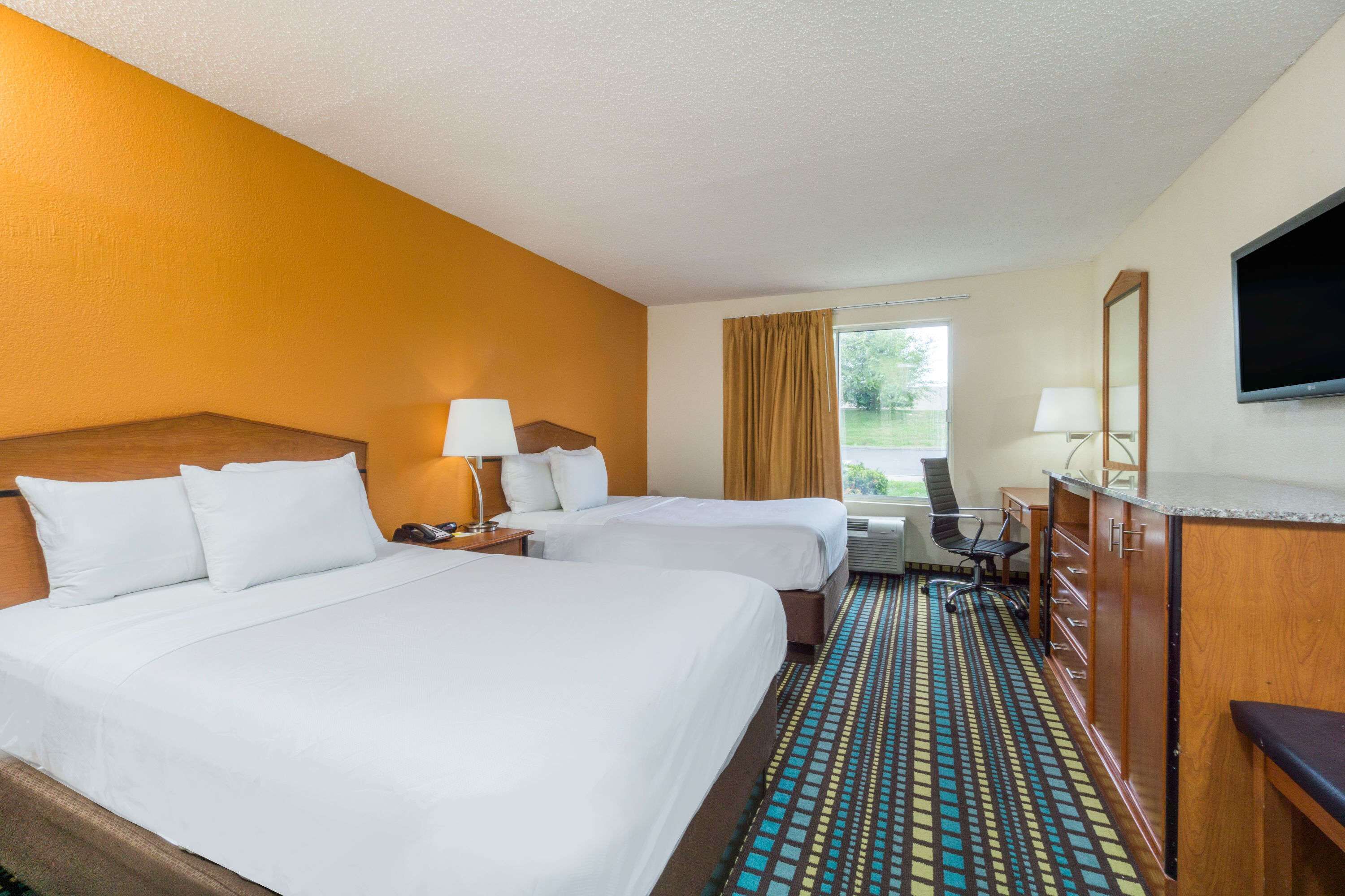A hotel room with two beds, a desk, a chair, a TV, and a window with curtains.