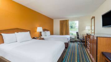 A hotel room with two beds, a desk, a chair, a TV, and a window with curtains.