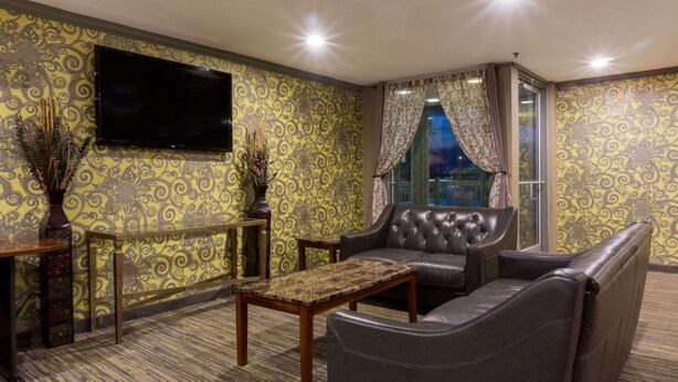 A room with patterned wallpaper, a flat-screen TV, leather seating, a small table, and a window with curtains. - Days Inn by Wyndham Florence Cincinnati Area (Florence)