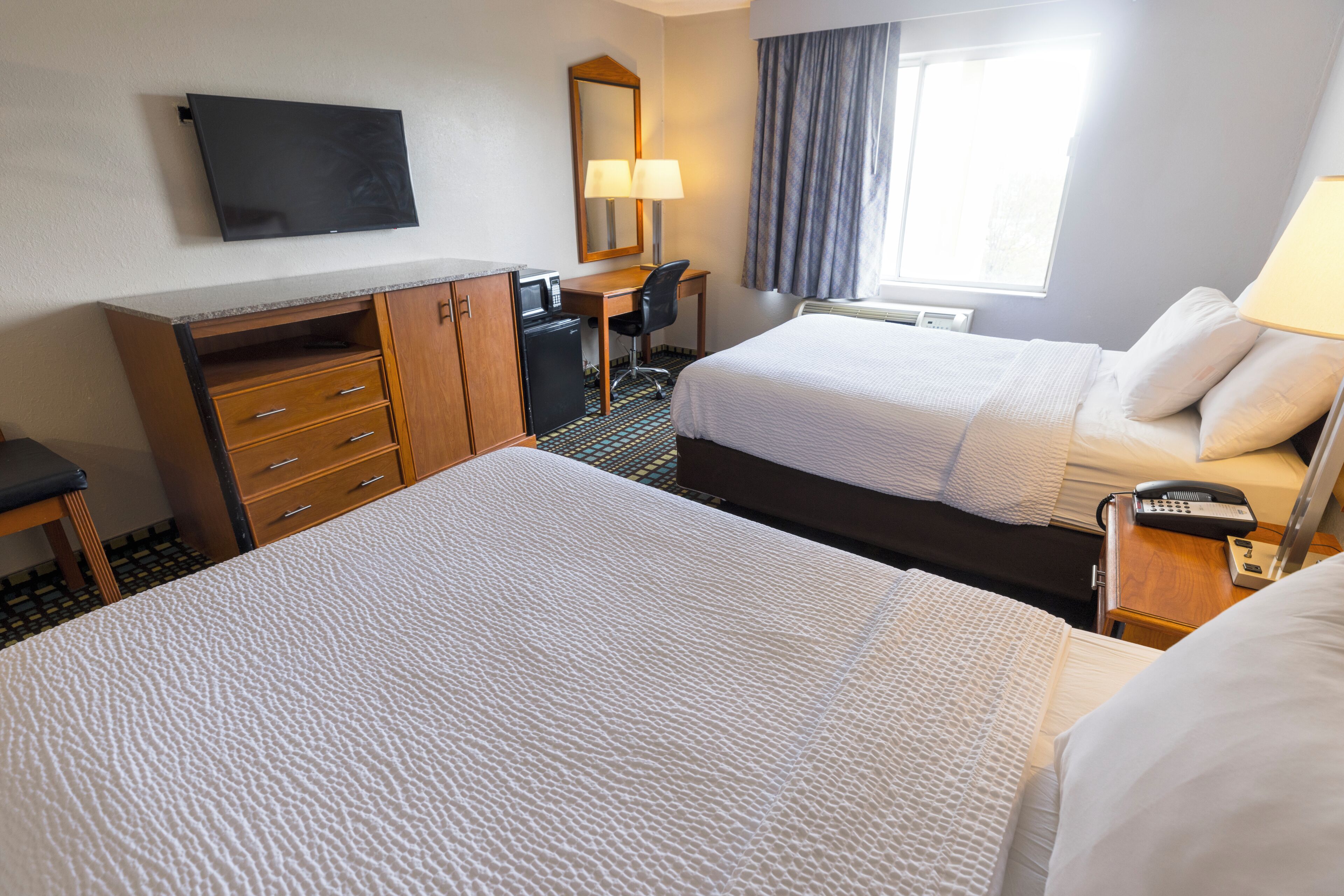 A hotel room with two beds, a desk, a chair, a TV, and a window with curtains.